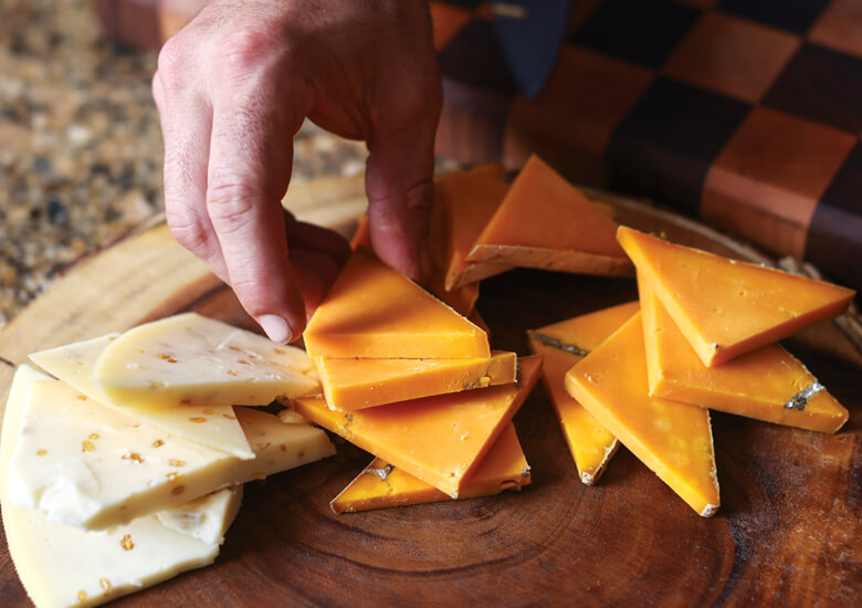 A hand reaches for small triangle-shaped pieces of cheese placed on a wooden plate